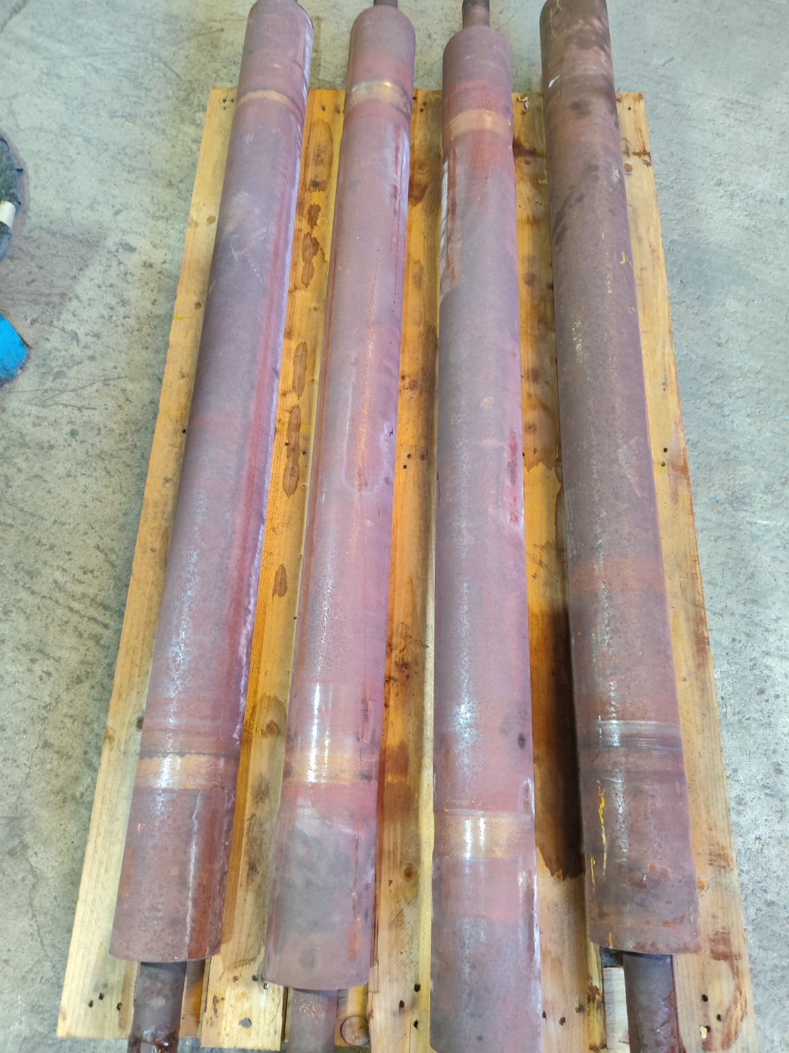 Cuatro rodillos industriales oxidados sobre un palé, antes de la limpieza láser